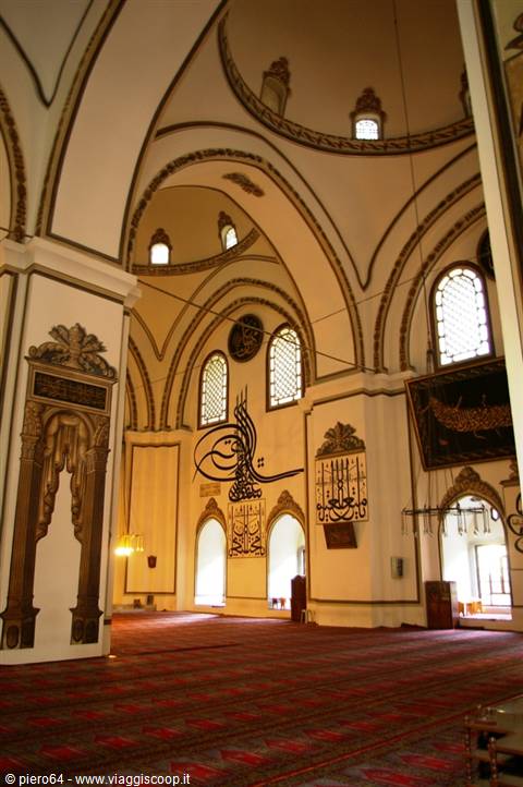 Inside Bursa's Great Mosque: pale vaults, calligraphy panels, red carpets, light through arched windows