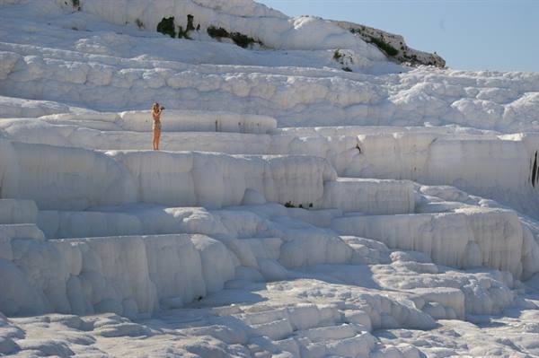 Tourist in swimsuit on white Pamukkale travertine terraces, bright sunlight