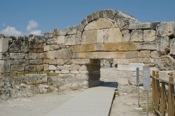 Ancient stone gate at Hierapolis, tourists walk through the arch in sunlight