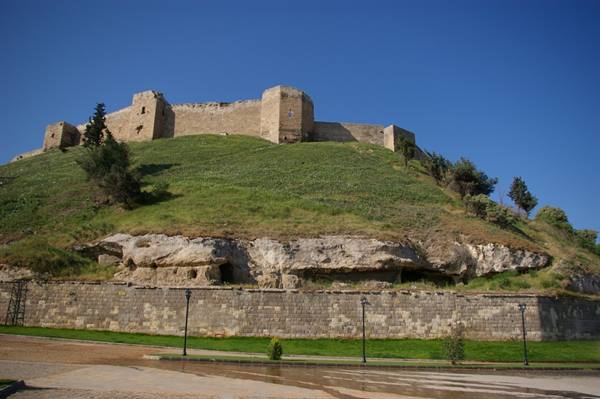 Gaziantep Citadel, stone walls on grassy hill under clear blue sky