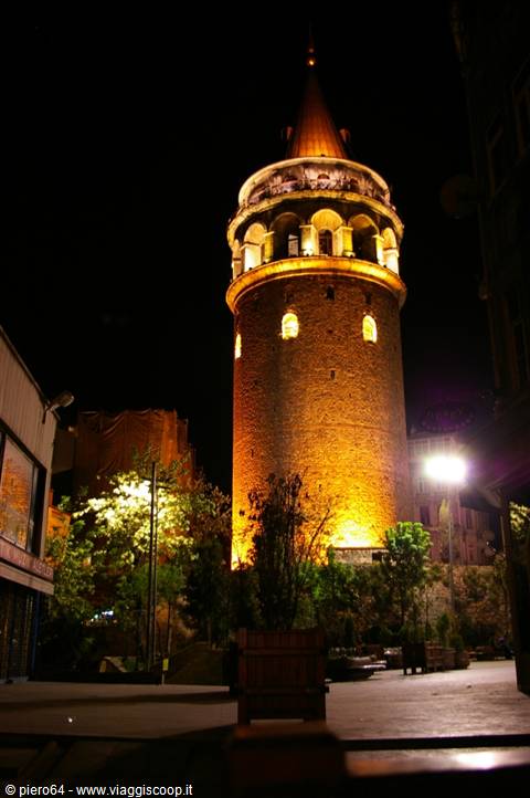 Galata Tower in Istanbul lit at night, golden stone among trees