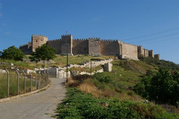 Crenellated walls of Ayasuluk Castle under blue sky, dirt road leading uphill