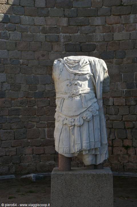 Headless marble statue of an armored Roman emperor against stone walls