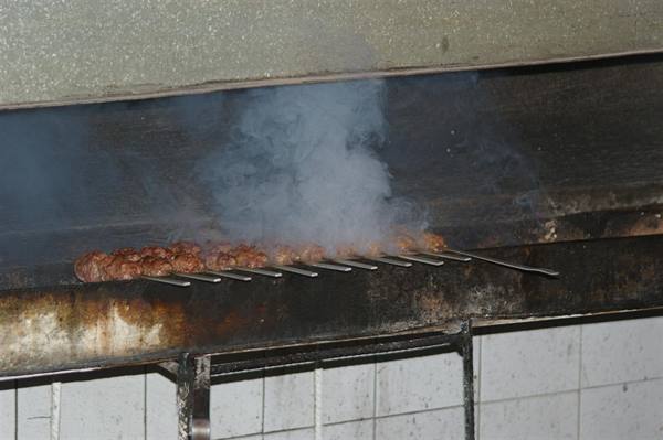 Meat skewers grilling on metal spit, thick smoke rising above