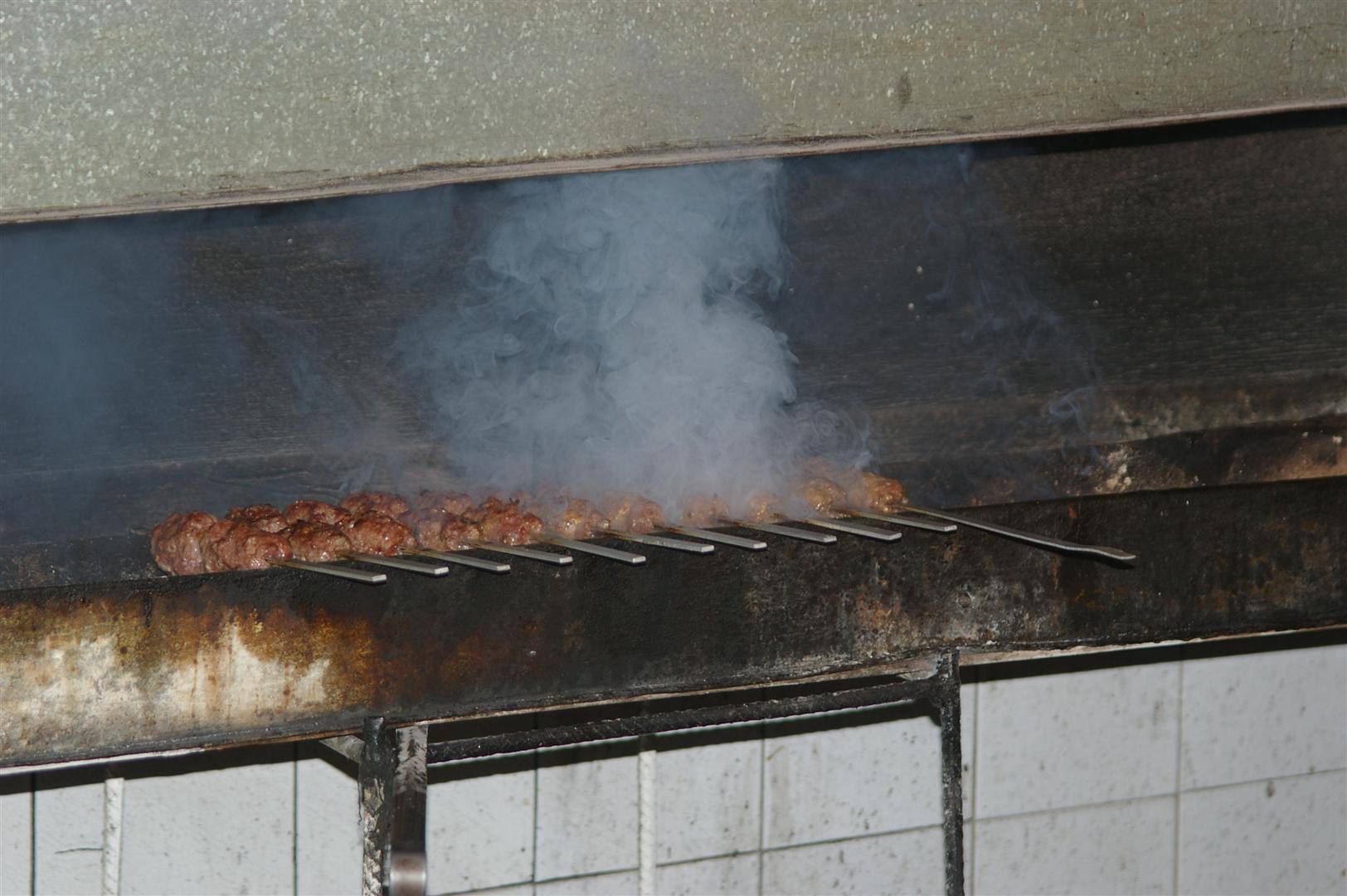 Spiedini di carne sui metalli della griglia, fumo denso sopra il fuoco