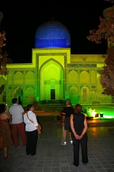 Tourists at night before the madrasa lit in green with blue dome in Samarkand
