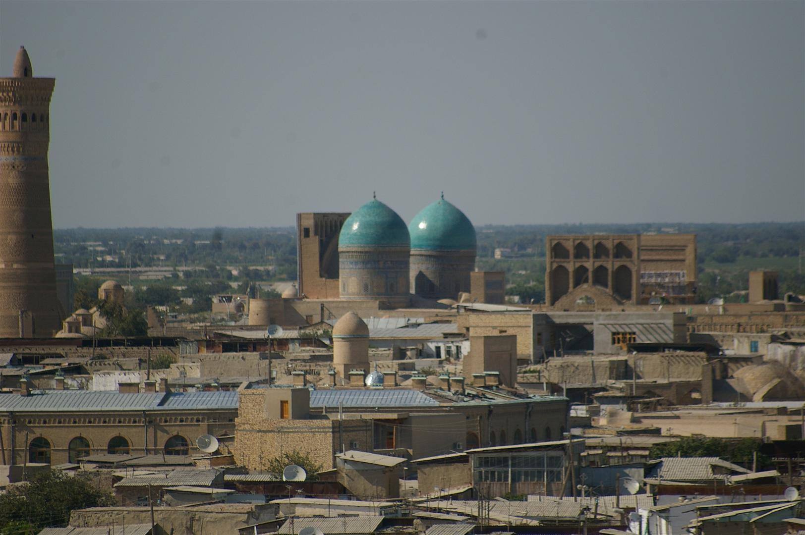 Bukhara: minareto in mattoni e cupole turchesi sopra i tetti antichi