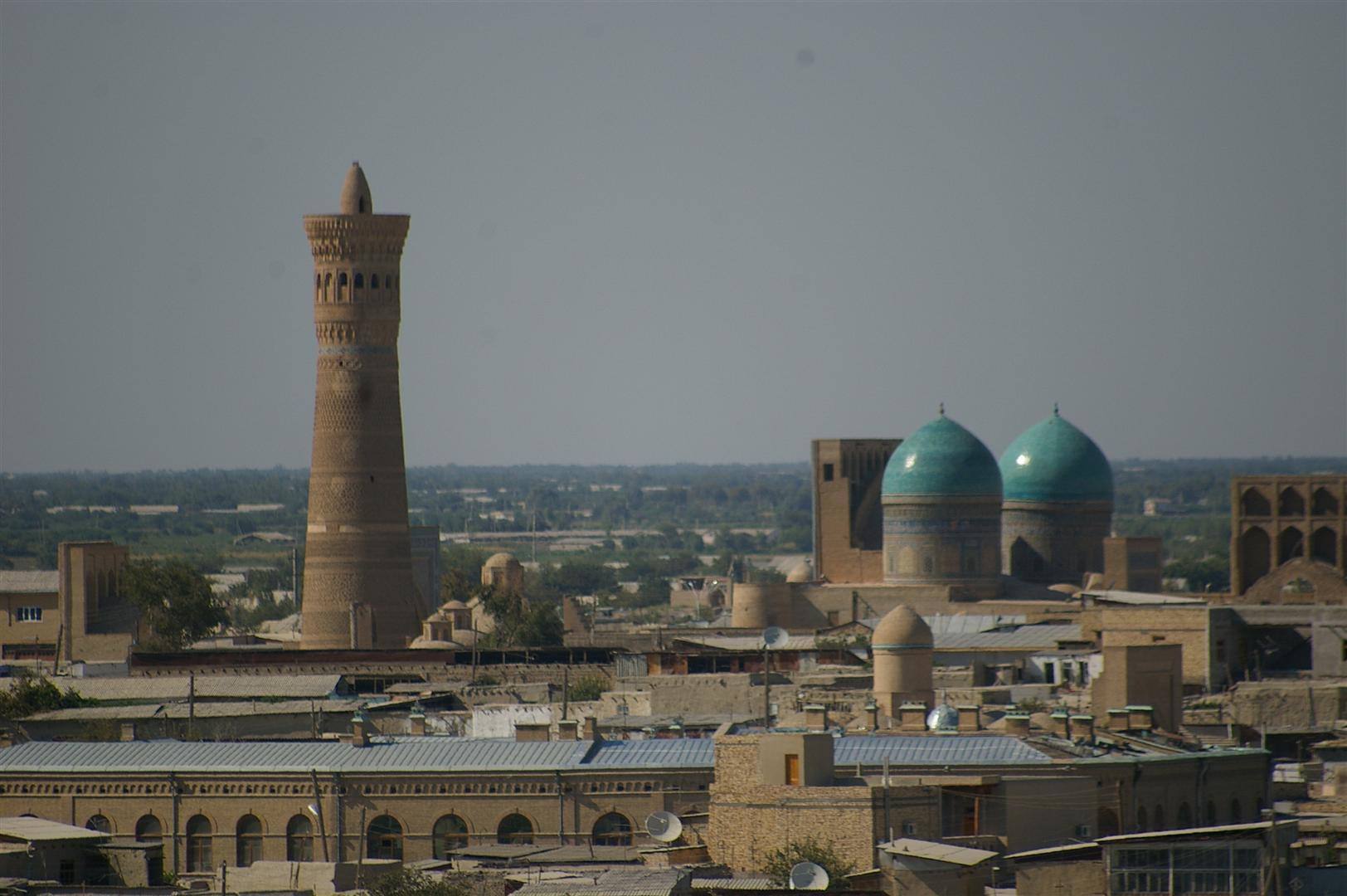 Minareto di mattoni e cupole turchesi sopra i tetti di Bukhara