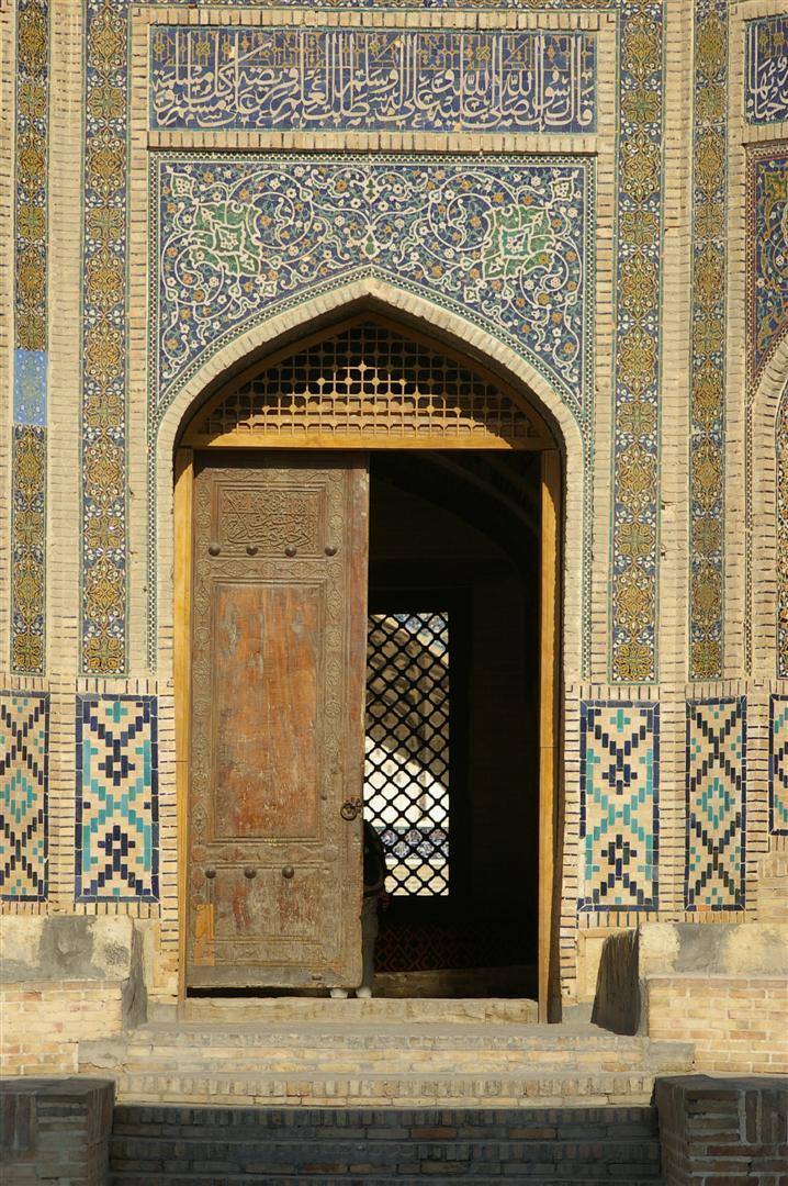 Porta in legno consumato sotto un arco ricoperto di maioliche blu e oro