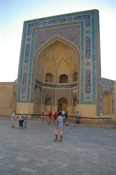 Tourists in front of the brick and blue tile portal of Bukhara madrasa