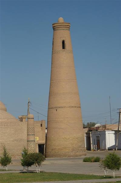 Brick minaret in Khiva, blue sky, white houses at its base