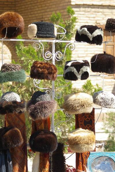 Fur hats hanging on a wrought iron display rack at a sunny outdoor market