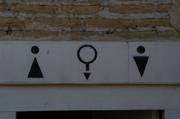 Painted restroom signs on a light brick wall, natural light