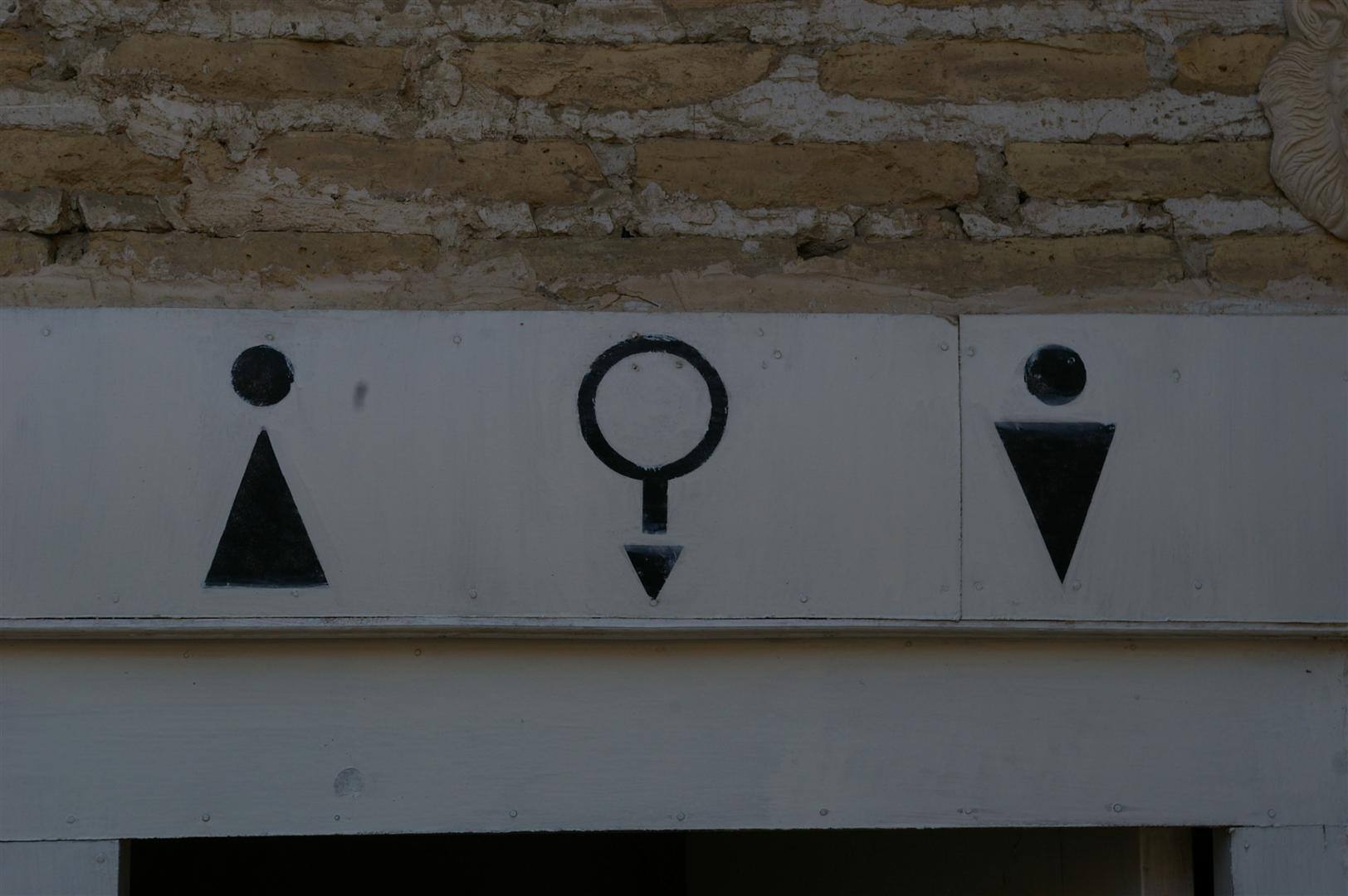Insegna dipinta di servizi igienici su muro di mattoni chiari, luce naturale