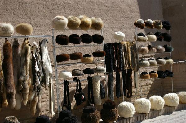 Fur hats and pelts displayed on metal racks against a sunlit brick wall