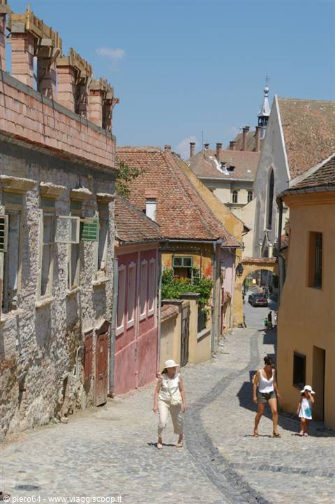 Women walk along cobbled street between colorful houses in Sighișoara