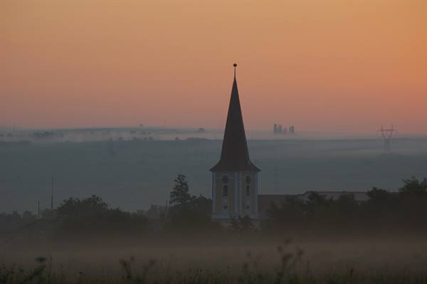 Church spire emerges from fog under an orange sky
