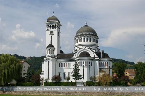 White Orthodox cathedral with dome and bell tower in Sighișoara, among trees and green hills
