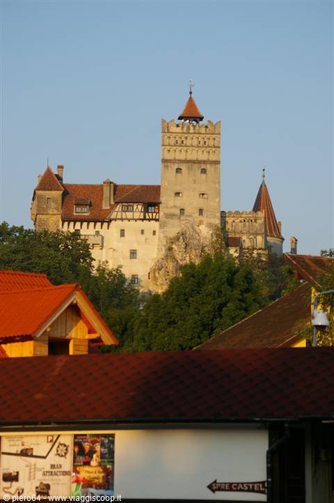 Bran Castle in stone and timber rises above red rooftops in clear morning light