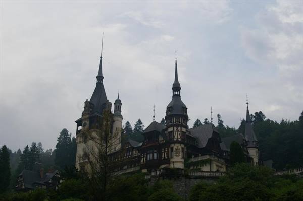 Peleș Castle in Sinaia, dark wooden spires among firs under cloudy sky