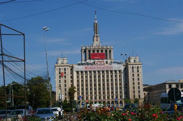 Casa Presei Libere with its spire, traffic and flowers under a blue sky