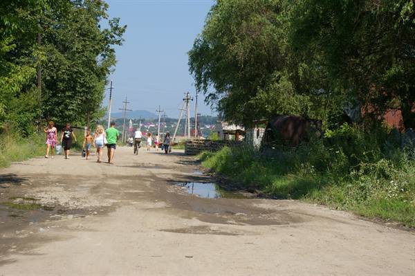 Tourists walk on a dirt road with puddles among trees and pylons