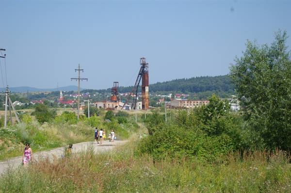 People walking on dirt road toward a rusty old mining headframe
