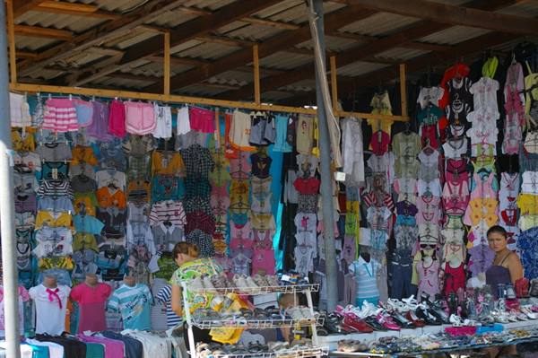 Open-air market stall with colorful hanging clothes and shoes
