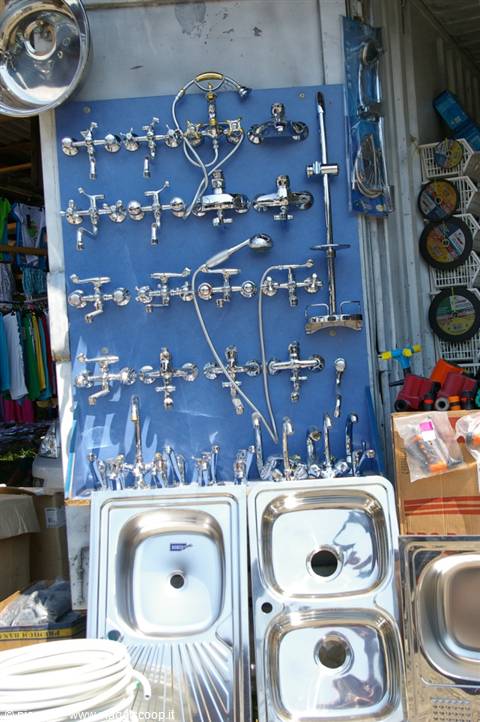 Chrome faucets and steel sinks displayed on a blue panel at an open-air market