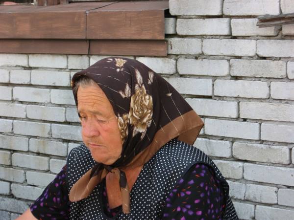 Elderly woman in a brown floral headscarf in front of a white brick wall