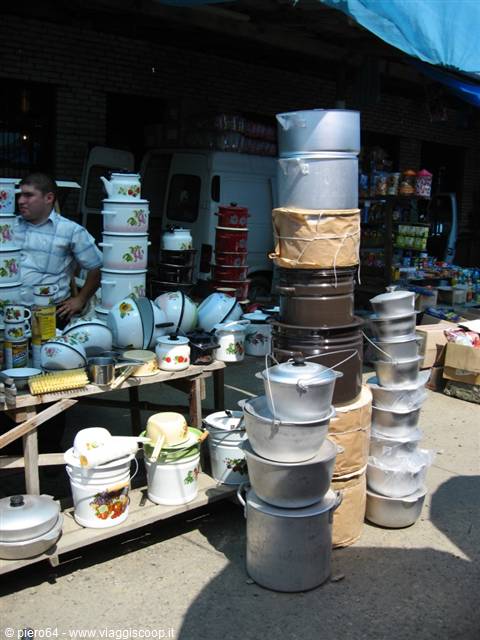 Outdoor market with stacked enamel and aluminum pots, vendor beside the stall