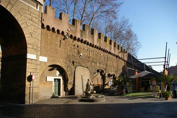 Sunlit brick crenellated wall with small fountain beneath a stone arch