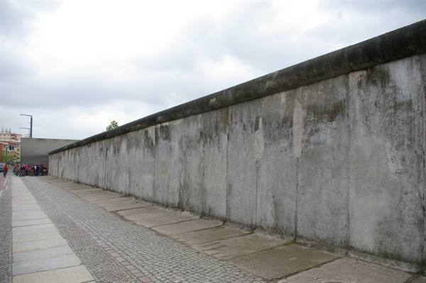 Berlin Wall concrete slab under cloudy sky, tourists on the left