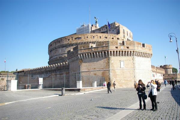Tourists photograph Castel Sant'Angelo in Rome under blue sky