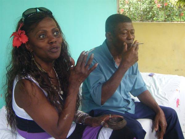 Woman with red flower in hair beside a man smoking on white sofa