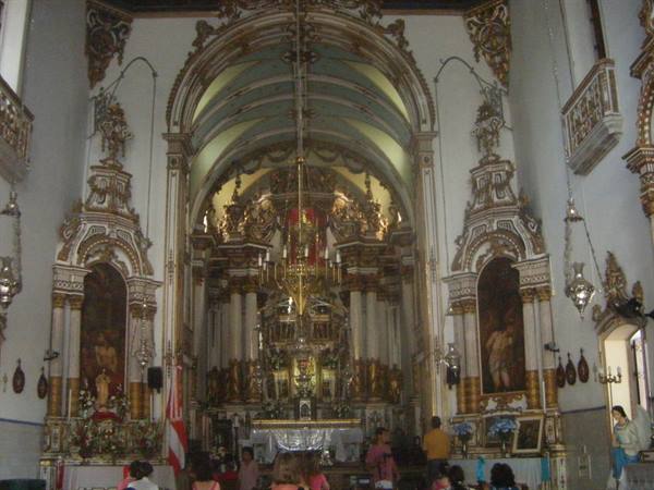 Gilded baroque high altar inside a church, visitors praying beneath the arch