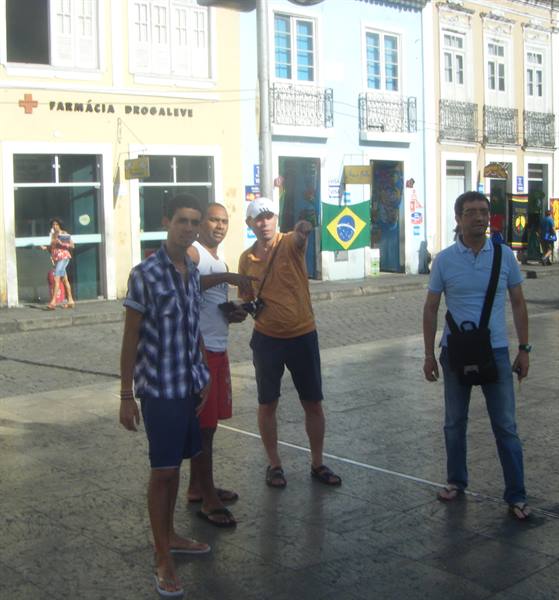 Tourists pose on a street in Salvador, one man pointing, Brazilian flag behind