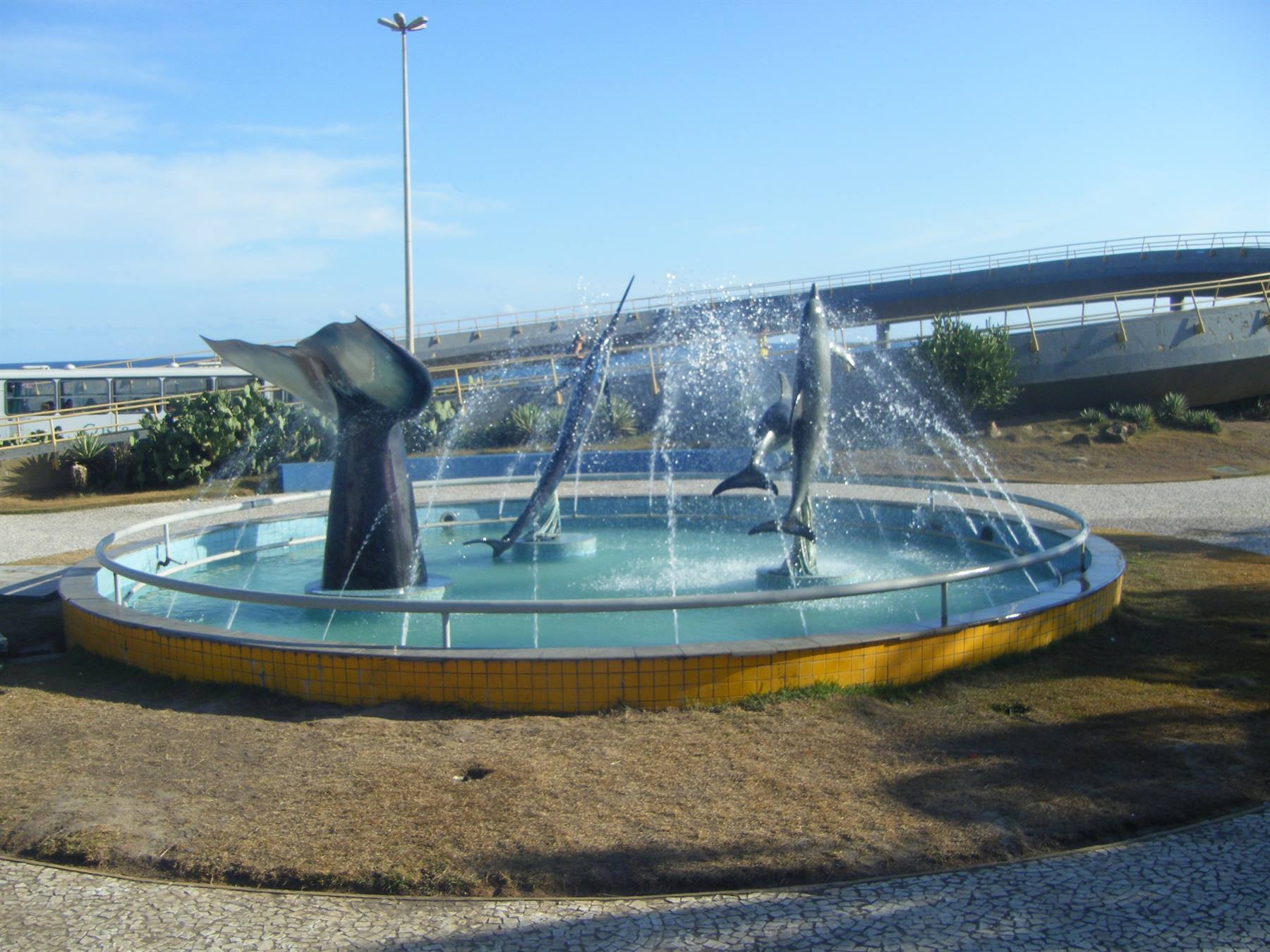 Round fountain with swordfish statues spraying water, yellow tiles