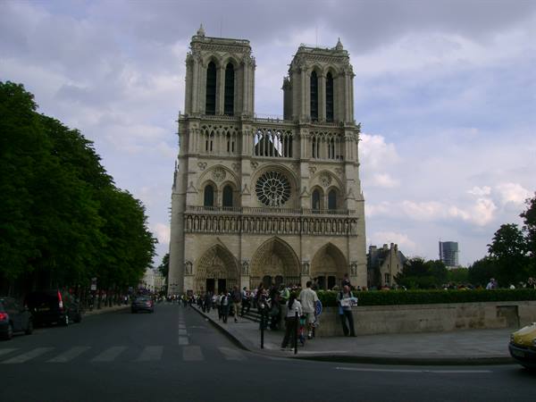 Tourists in front of Notre-Dame's Gothic facade in Paris, cloudy sky
