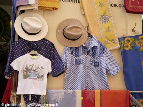 Straw hats and printed shirts hanging at a Provencal market stall