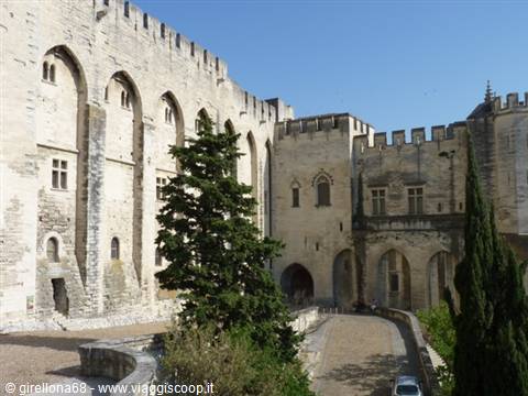 Crenellated walls of the Papal Palace in Avignon, pale stone under sun, cypresses