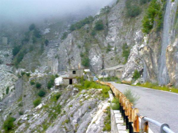 Road beside white marble quarries, rusty guardrail and fog over the Apuan Alps