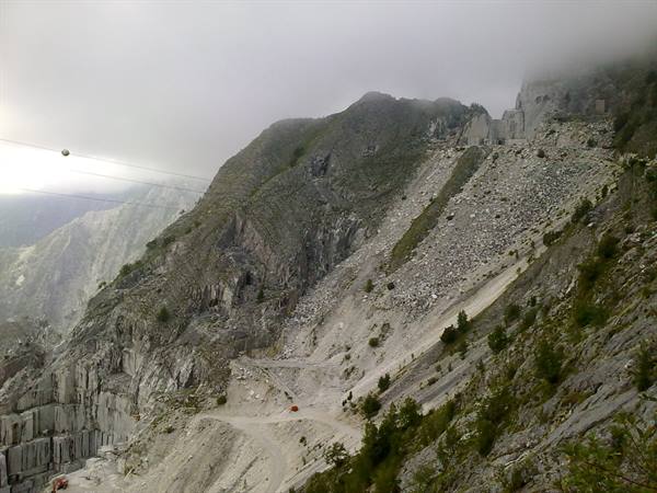 Carrara marble quarry: carved white walls, rubble slopes, cable line in the mist