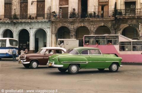 Green and brown vintage cars in front of an arcaded building in Havana