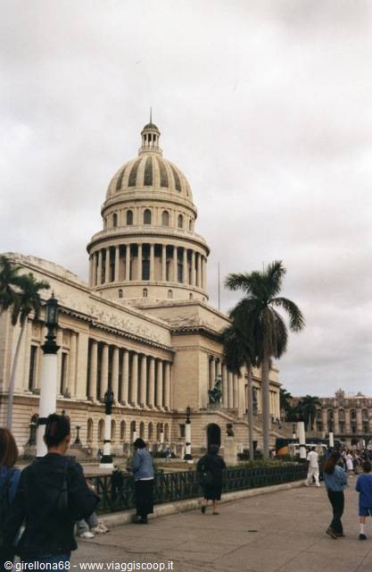 Tourists walk past Havana's Capitolio among palm trees under a grey sky
