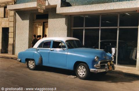 Vintage blue car with white roof parked in front of a shop