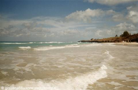 White waves on sandy beach, green rocky shore under cloudy sky