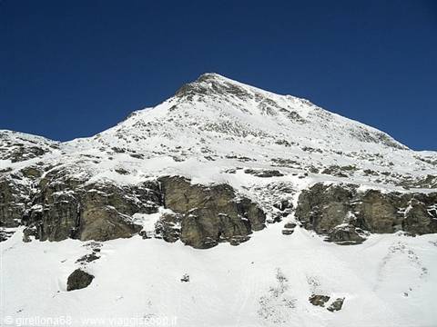 Snow-covered rocky peak under deep blue sky, bright snow on cliffs
