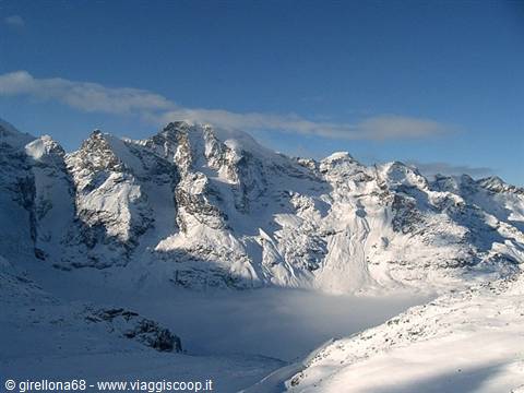 Snow-covered rocky peaks under blue sky, fog in the icy valley
