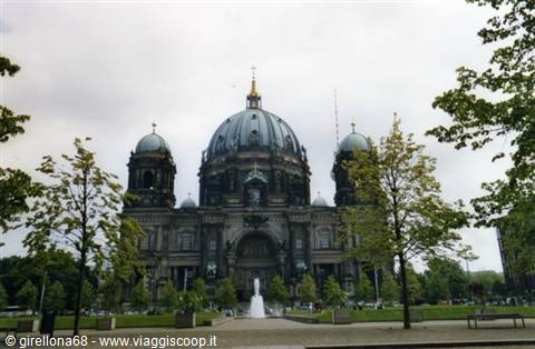 The green dome of Berlin Cathedral framed by trees, fountain in front
